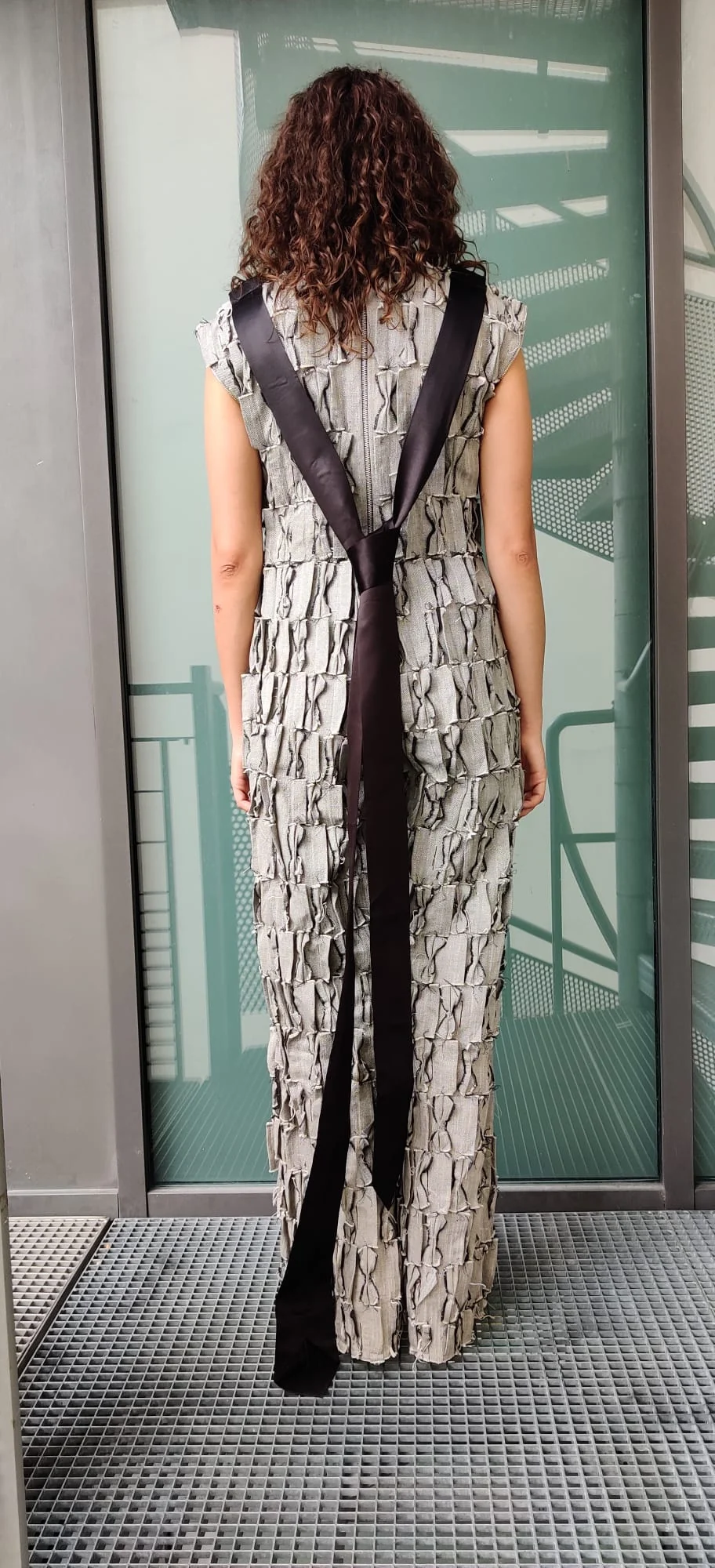 Managerial Grace photographed from behind, showing the crossed satin ties against the jumpsuit's woven surface