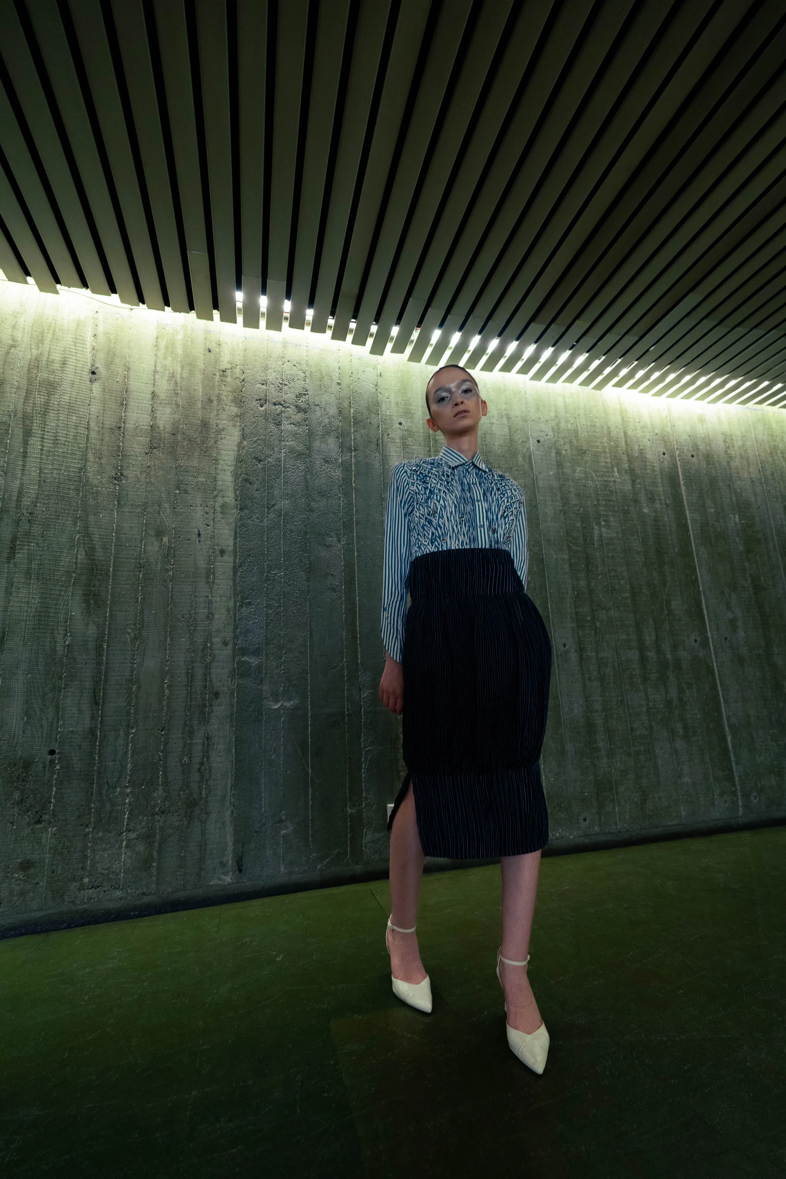 The Paralegal Fit photographed in a lit corridor at Espace Niemeyer, showing the smocked bodice and pinstripe balloon skirt with its side slit